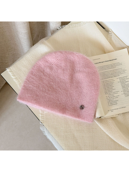 Light Pink fuzzy knit beanie with visible crown seams and a small silver-tone emblem near the lower edge.