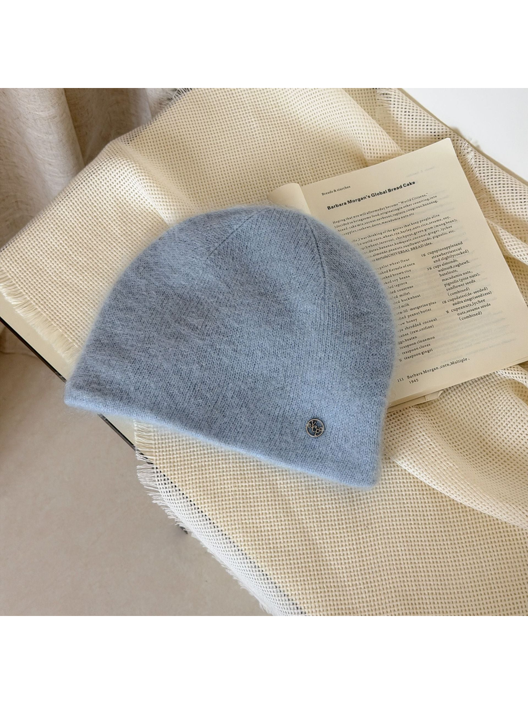 Light Blue fuzzy knit beanie with a rounded crown and small silver-tone emblem.