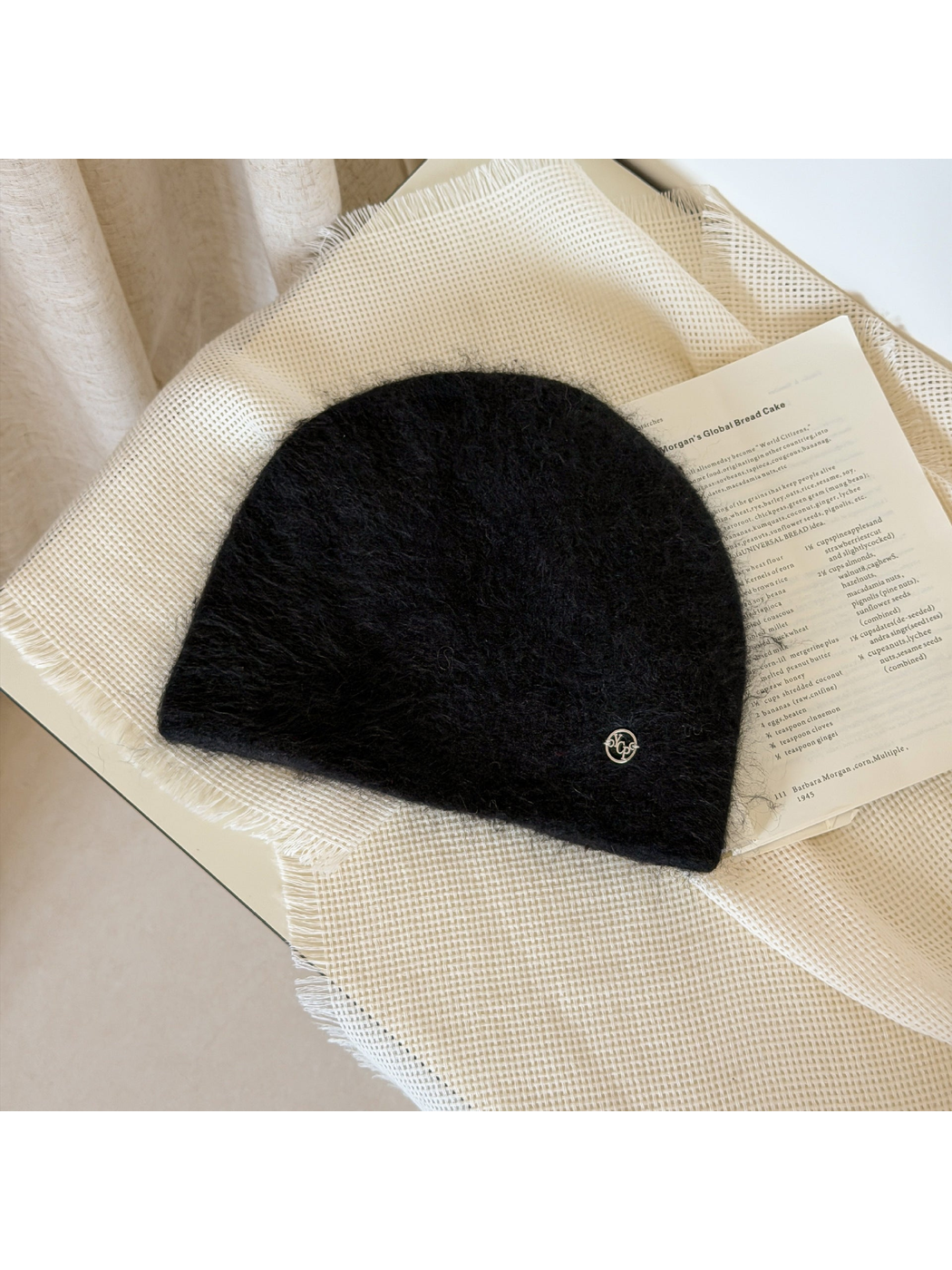Black fuzzy knit beanie with a rounded crown and small silver-tone emblem.