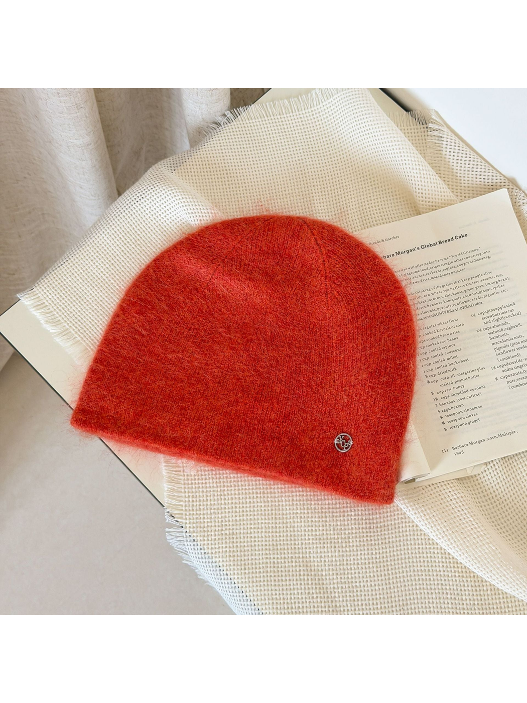 Orange Red fuzzy knit beanie with a rounded crown and small silver-tone emblem.