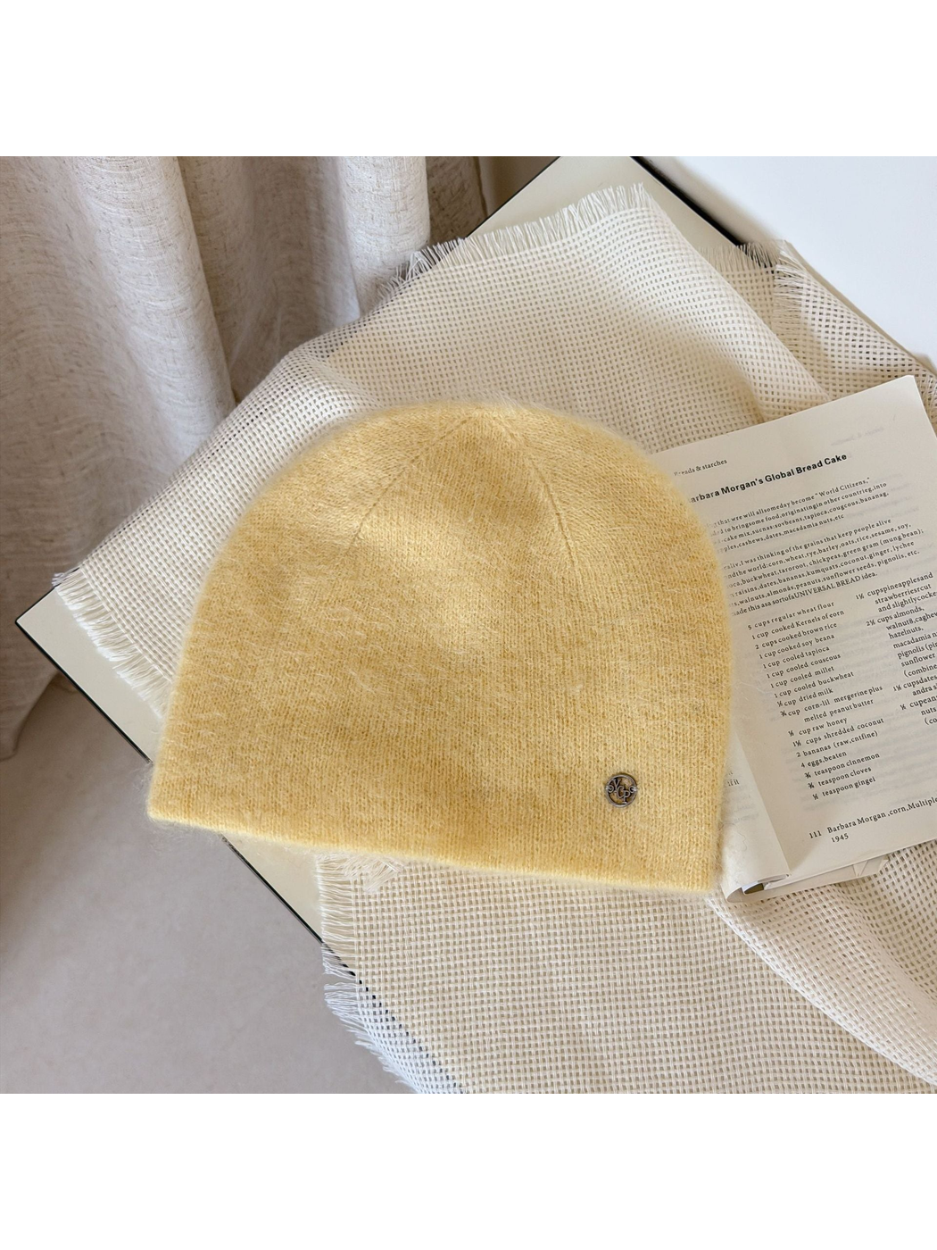 Yellow fuzzy knit beanie with a rounded crown and small silver-tone emblem.