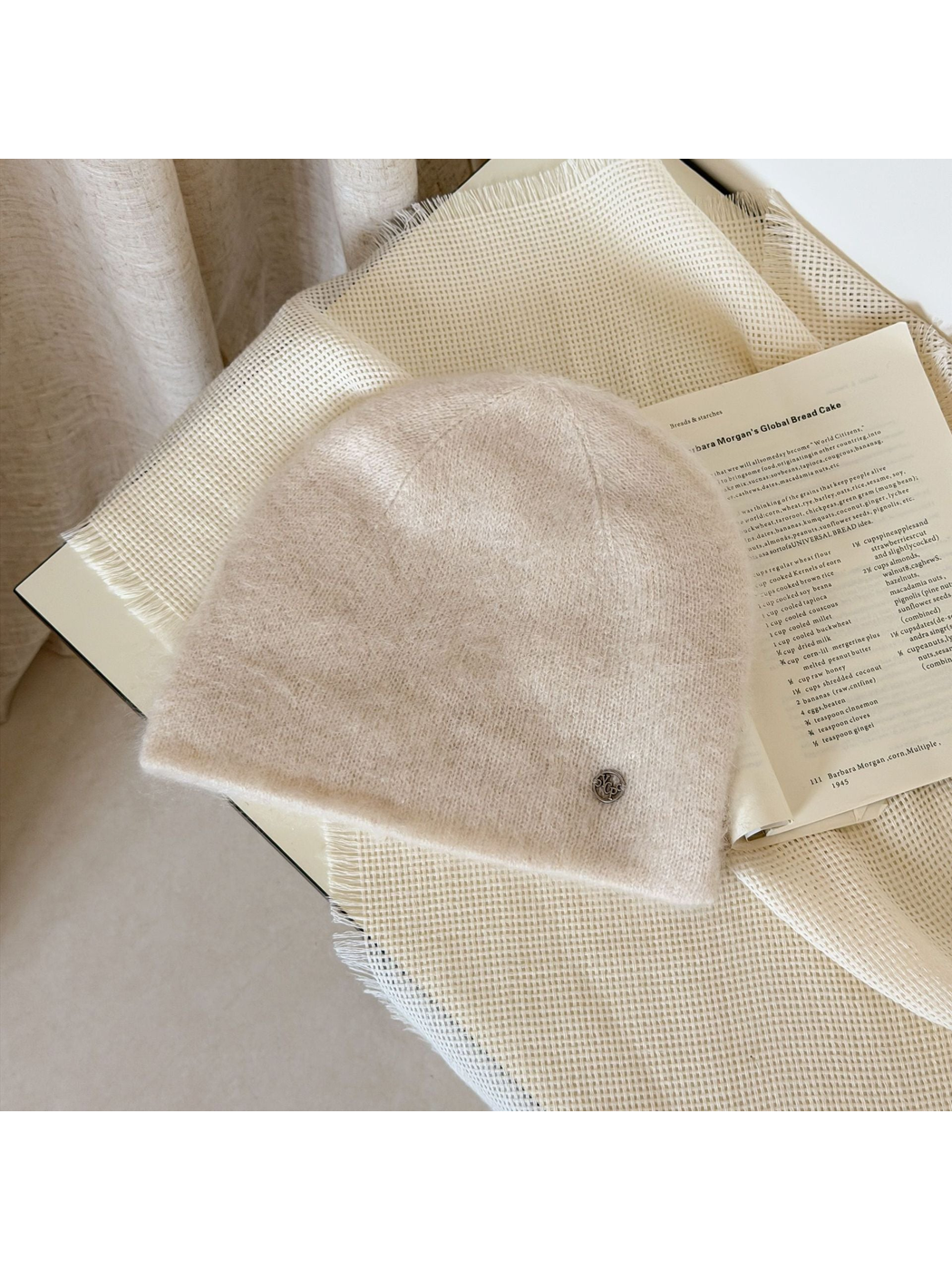 Ivory fuzzy knit beanie with a rounded crown and small silver-tone emblem.