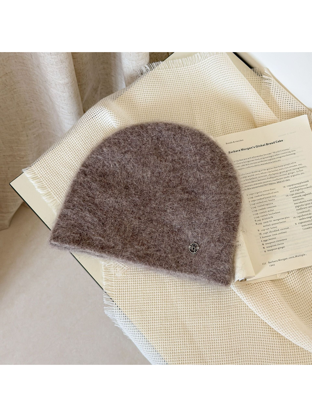 Light Coffee fuzzy knit beanie with a rounded crown and small silver-tone emblem.