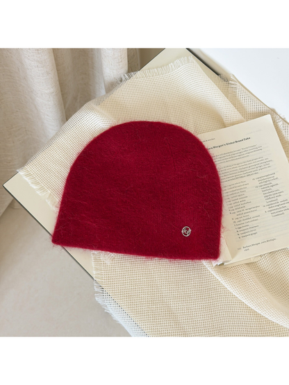 Burgundy fuzzy knit beanie with a rounded crown and small silver-tone emblem.
