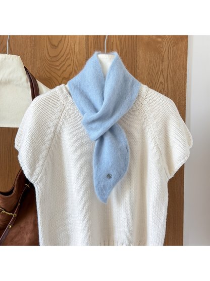 Sky Blue fuzzy knit scarf looped over a white knit top, with a tapered end and round silver-tone emblem.