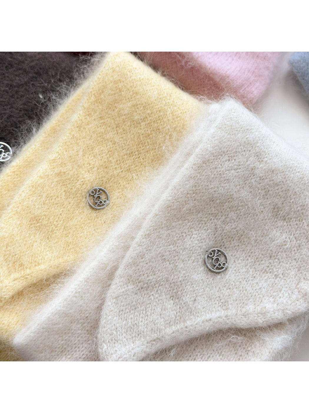 Close-up of Yellow and Ivory scarves showing fuzzy knit texture and round silver-tone emblems.
