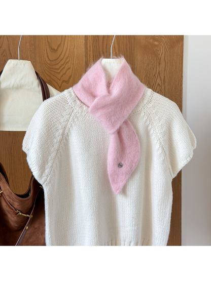 Light Pink fuzzy knit scarf looped over a white knit top, with a tapered end and round silver-tone emblem.