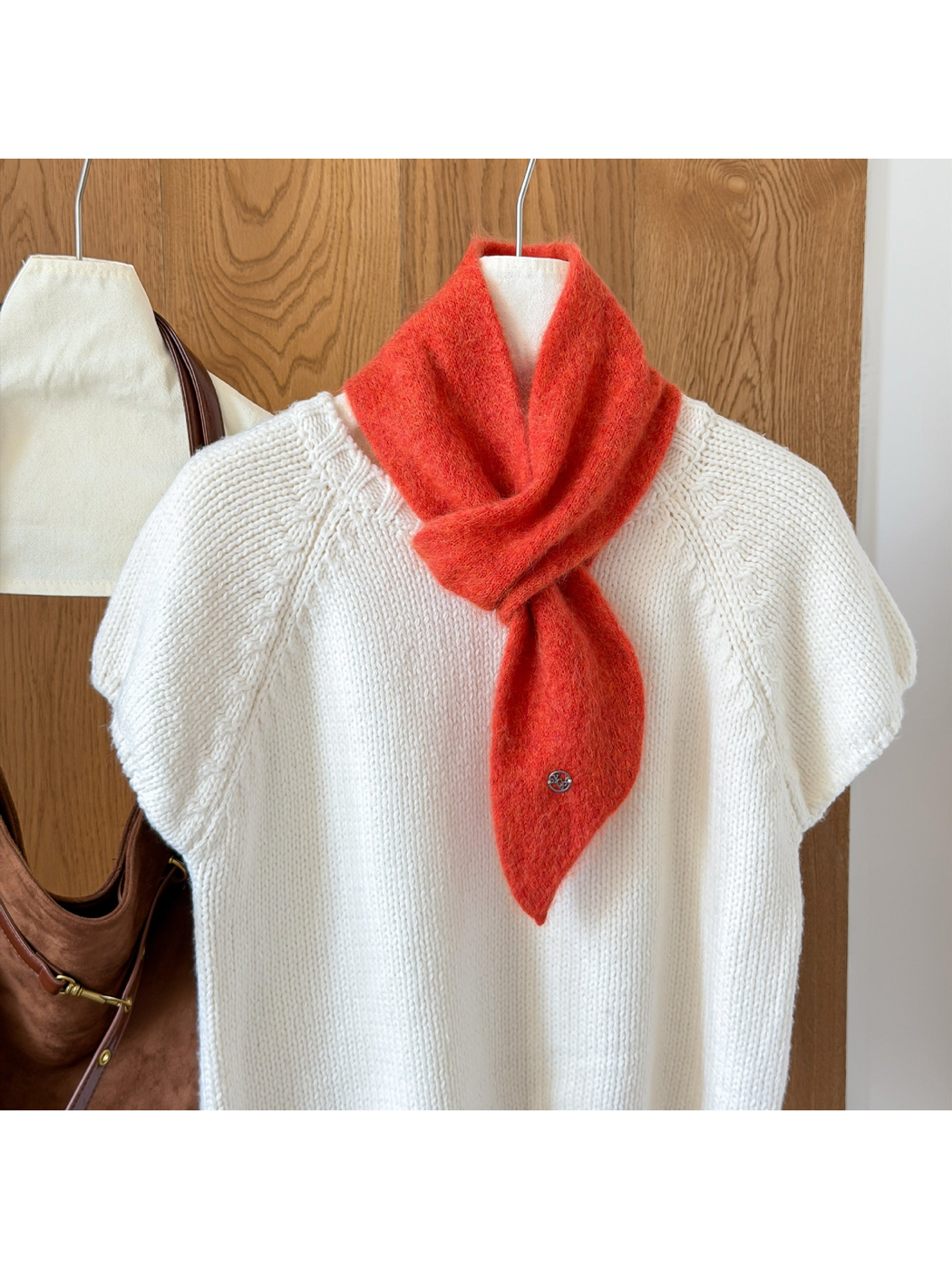 Orange Red fuzzy knit scarf looped over a white knit top, with a tapered end and round silver-tone emblem.