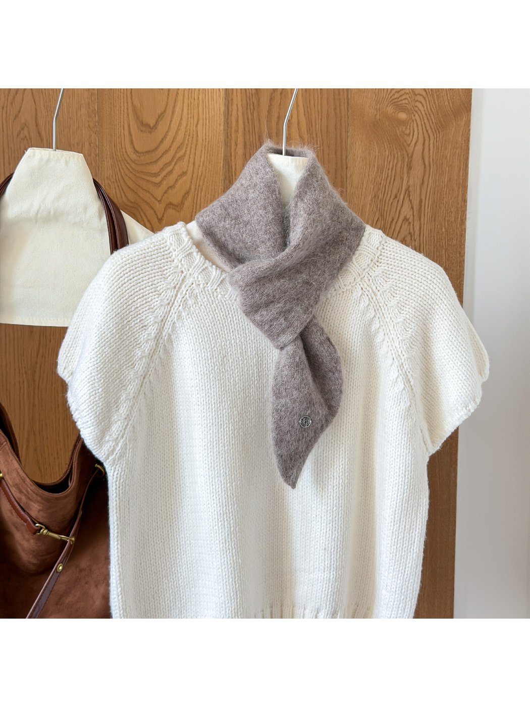 Light Coffee fuzzy knit scarf looped over a white knit top, with a tapered end and round silver-tone emblem.