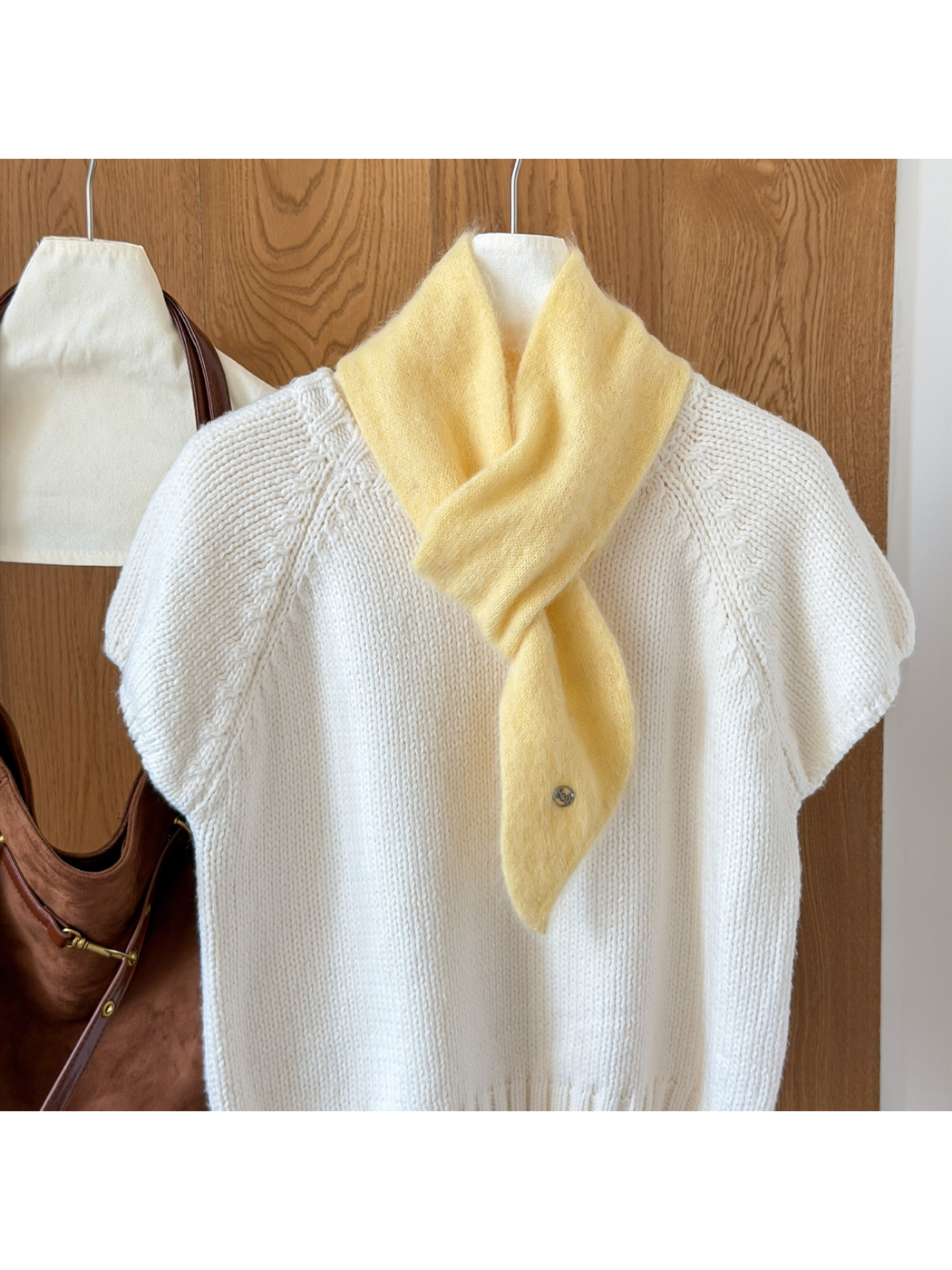Yellow fuzzy knit scarf looped over a white knit top, with a tapered end and round silver-tone emblem.