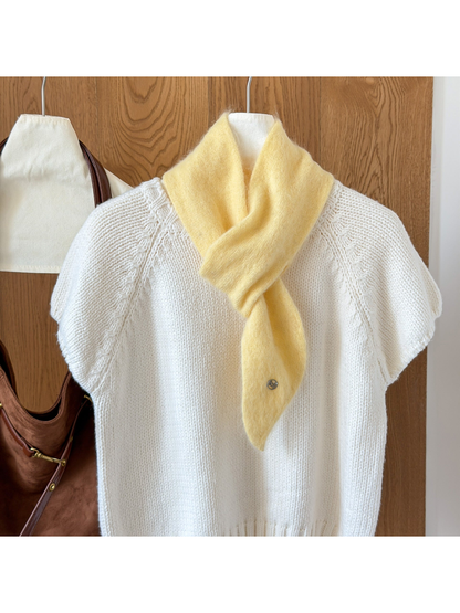 Yellow fuzzy knit scarf looped over a white knit top, with a tapered end and round silver-tone emblem.