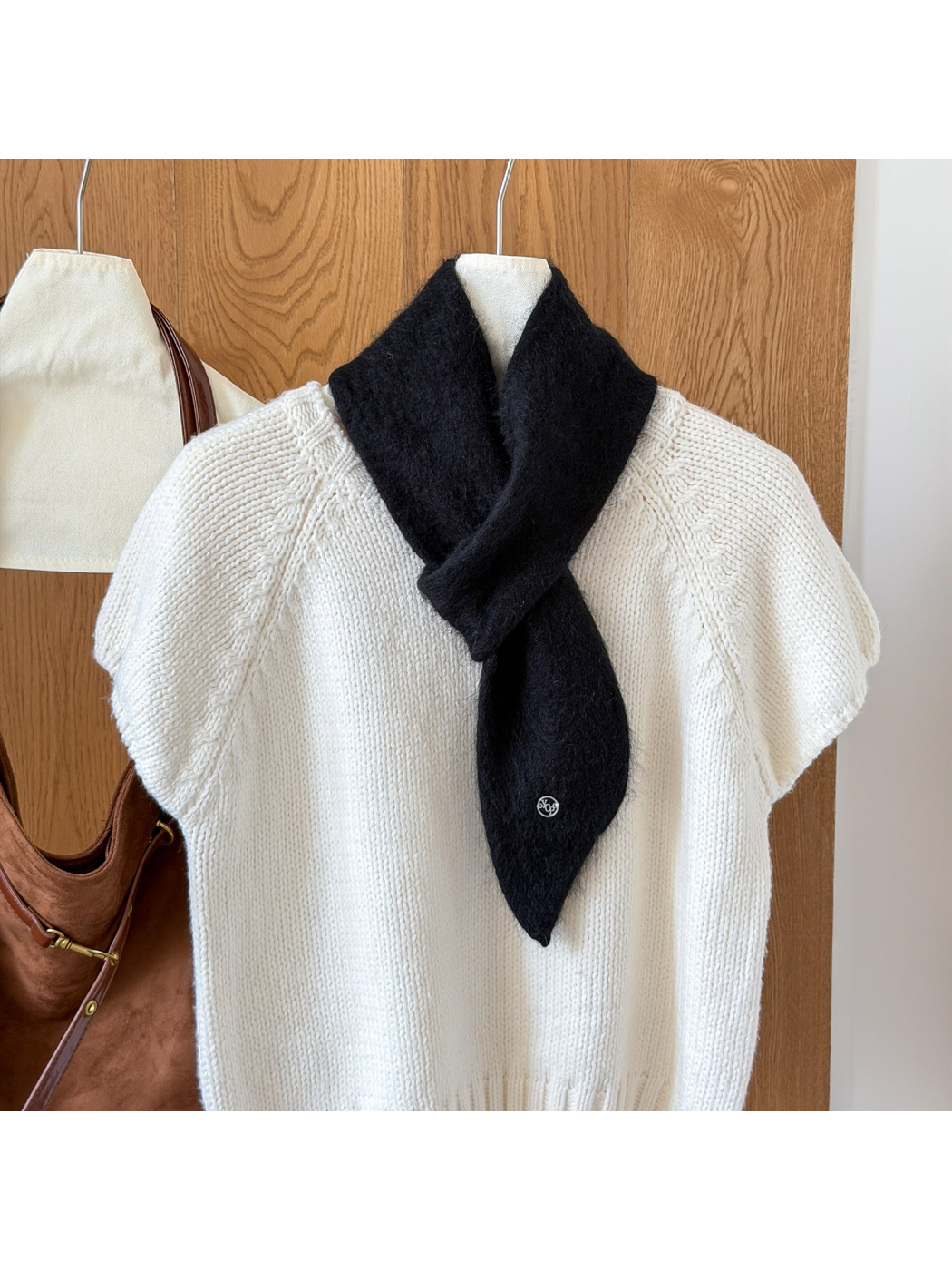Black fuzzy knit scarf looped over a white knit top, with a tapered end and round silver-tone emblem.
