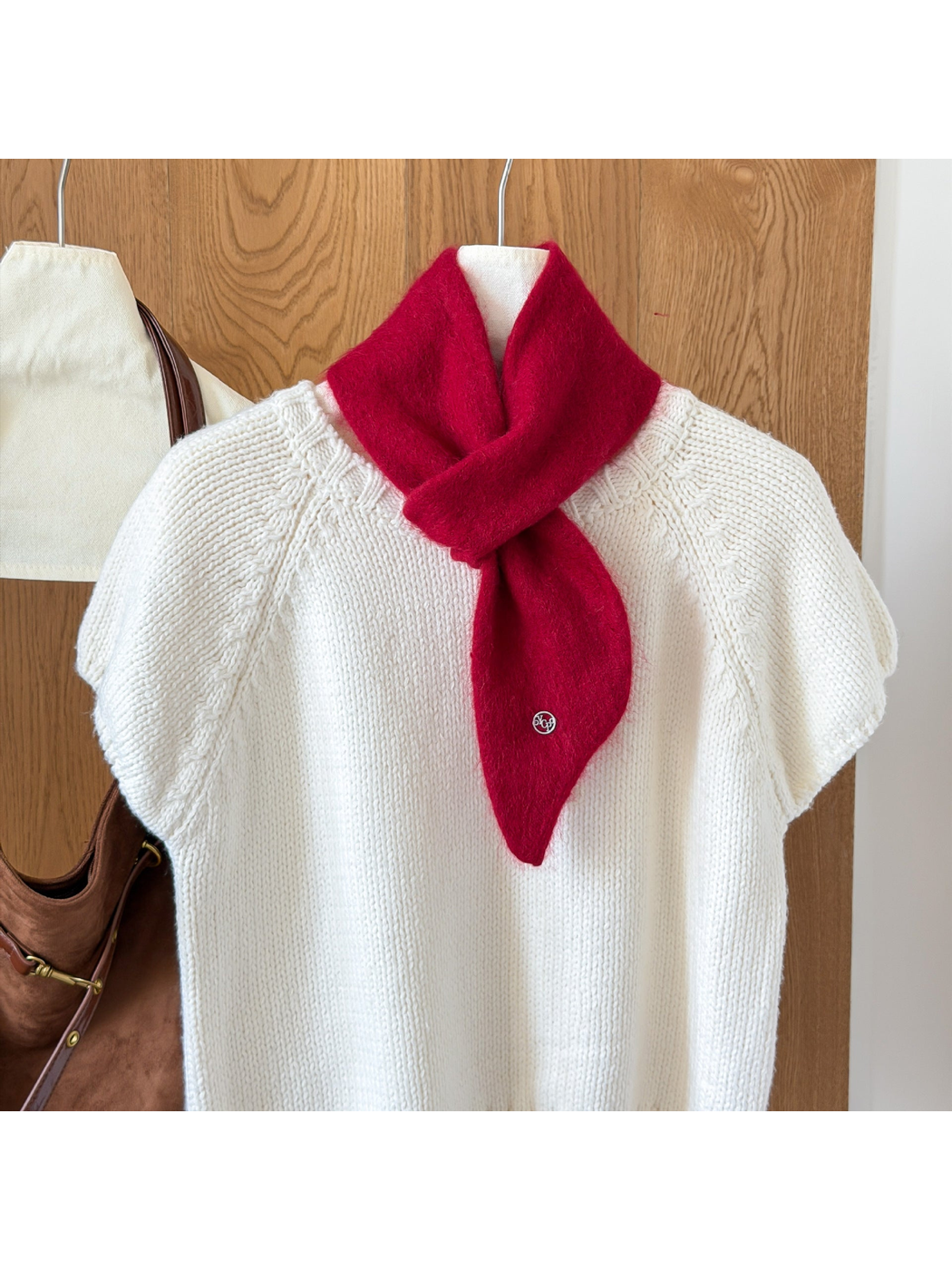 Burgundy fuzzy knit scarf looped over a white knit top, with a tapered end and round silver-tone emblem.