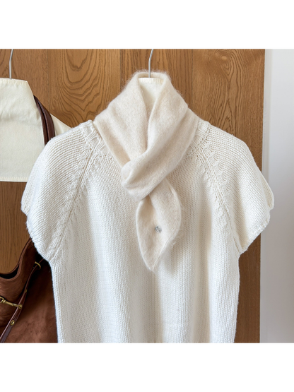 Ivory fuzzy knit scarf looped over a white knit top, with a tapered end and round silver-tone emblem.