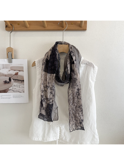 Gray floral patchwork scarf looped over a white top.