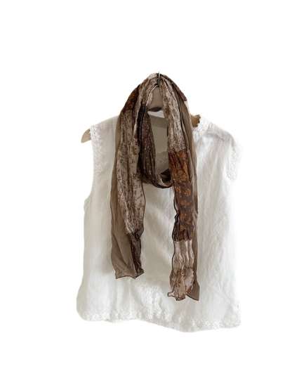 Khaki floral patchwork scarf draped in a long loop over a white top.