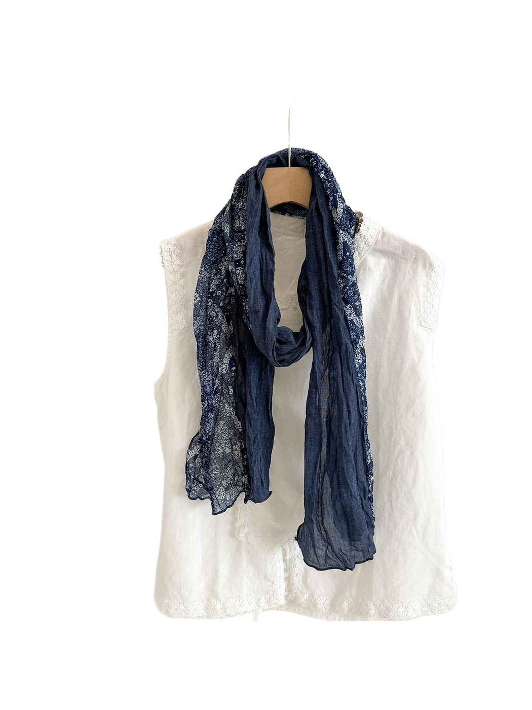 Navy scarf with solid blue and white paisley sections, looped over a white top against a white background.