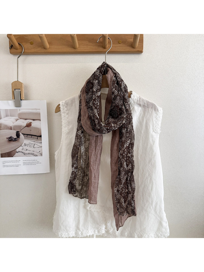 Coffee scarf with pale paisley motifs and contrasting solid sections, looped over a white top.