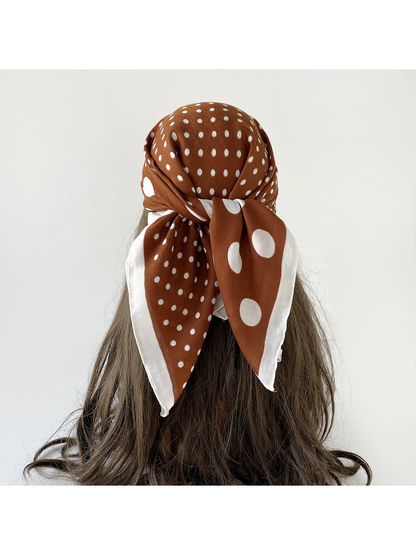 Brown polka dot scarf worn over the head and tied at the back, with white-bordered ends over long hair.