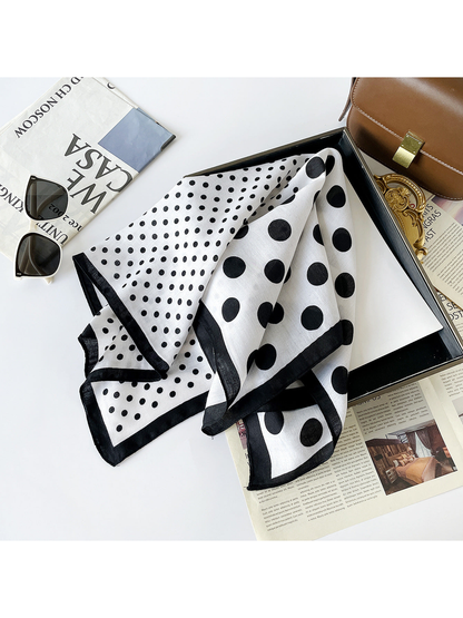 White scarf with large and small black polka dots loosely draped across a tray beside sunglasses.