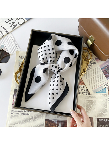 White polka dot scarf tied into a loop in a tray held by a hand, with black-bordered ends.