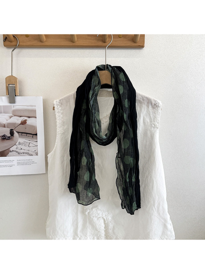 Green polka dot scarf looped over a white blouse on a hanger.