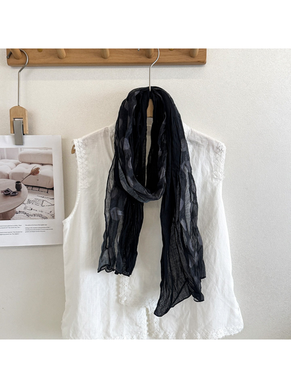 Black scarf with gray polka dots draped in a loop over a white blouse.