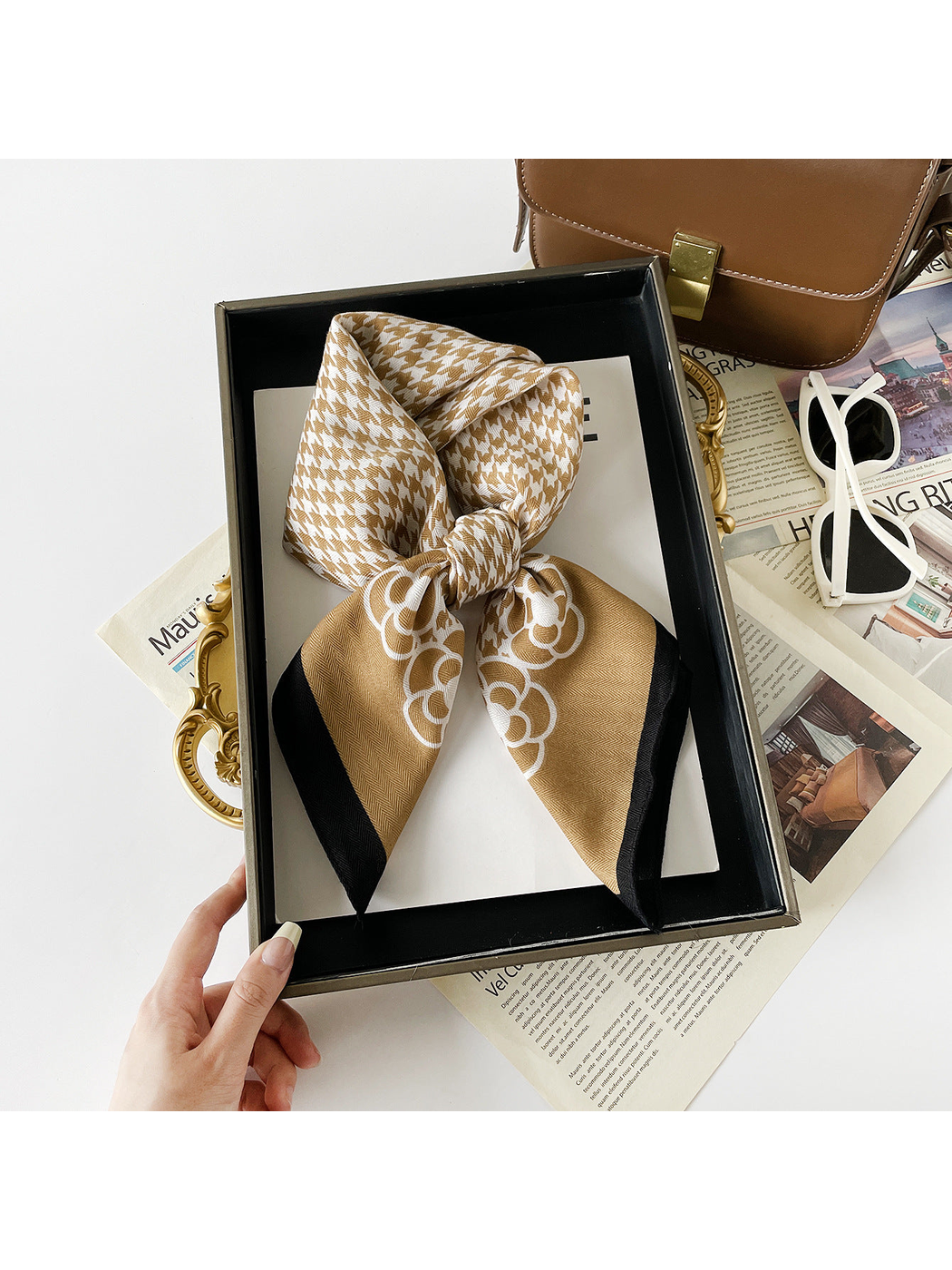 Camel scarf arranged in a knotted loop with white floral motifs and black edging.