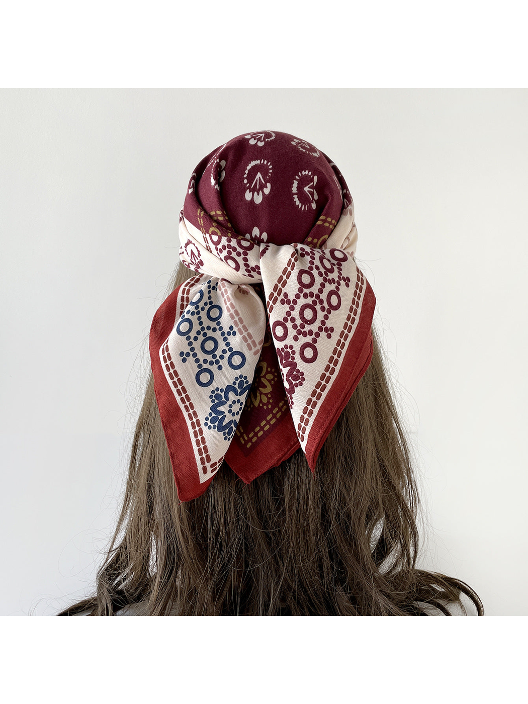 Burgundy patterned scarf worn as a headscarf and tied at the back over long hair.
