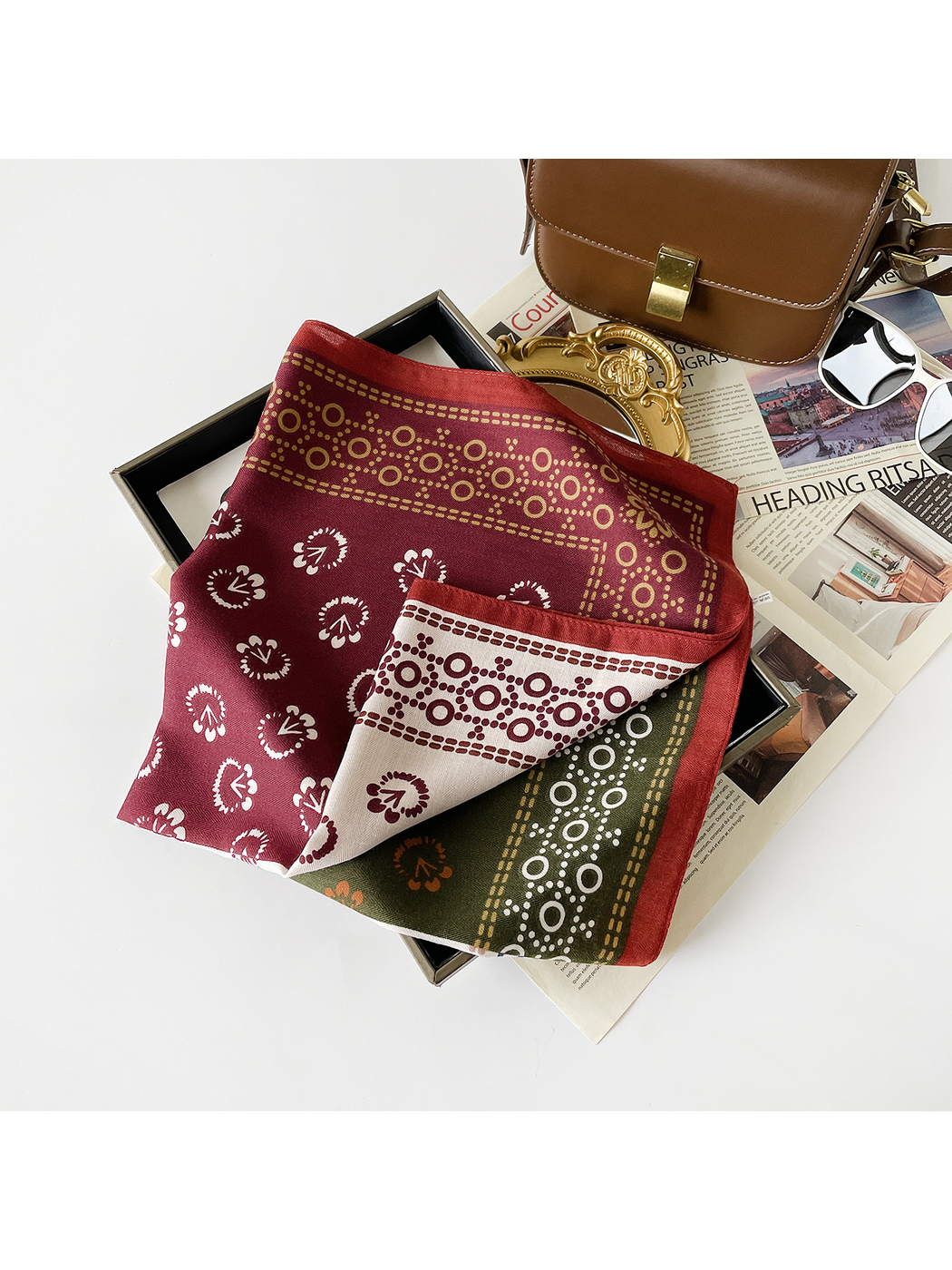 Burgundy scarf loosely folded in a tray, revealing cream and olive panels beneath its patterned border.