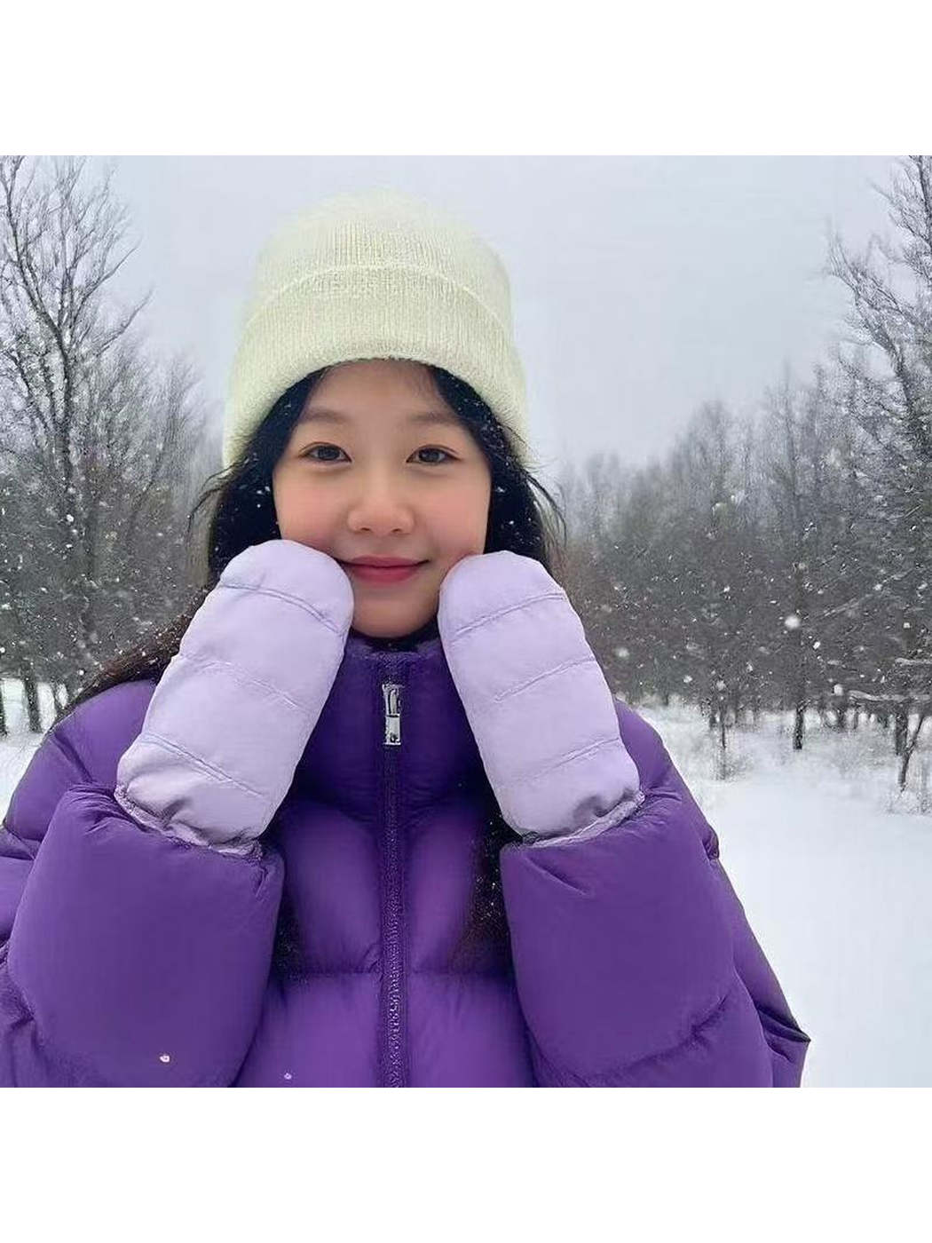 Person wearing purple mittens held against their cheeks in a snowy setting.