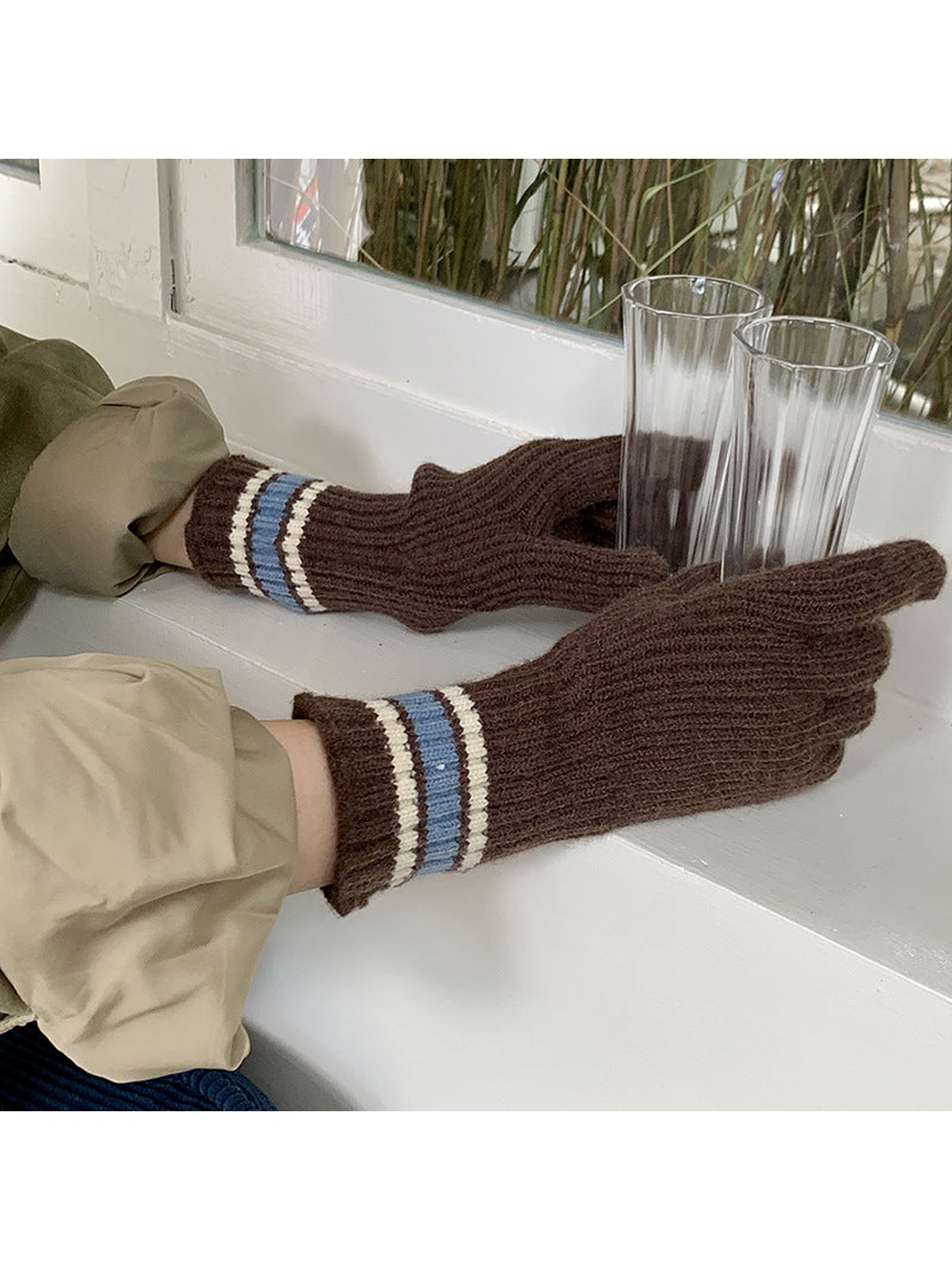 Gloves with Blue / Ivory striped cuffs worn while holding two tall drinking vessels by a window.
