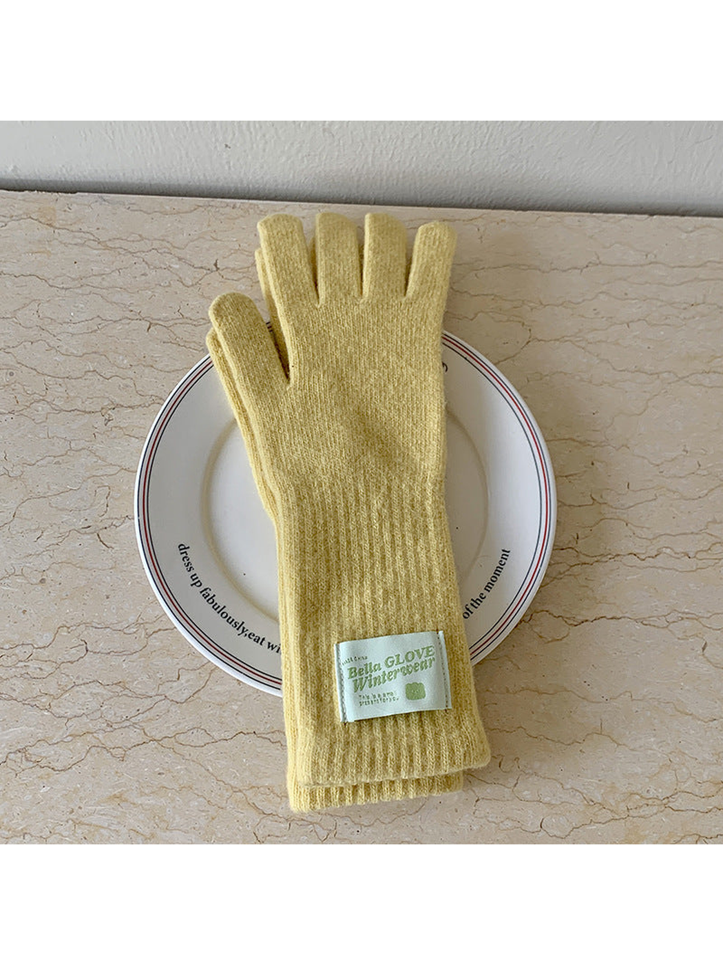 Mustard Yellow knit gloves with long ribbed cuffs and a pale green label, arranged on a plate.
