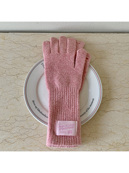 Dusty Pink knit gloves with long ribbed cuffs and a pink label, arranged on a plate.
