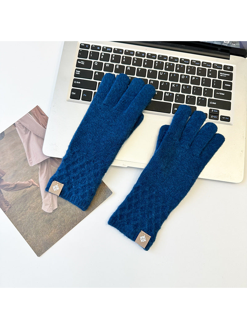 Blue knit gloves with diamond lattice cuffs arranged beside a laptop.