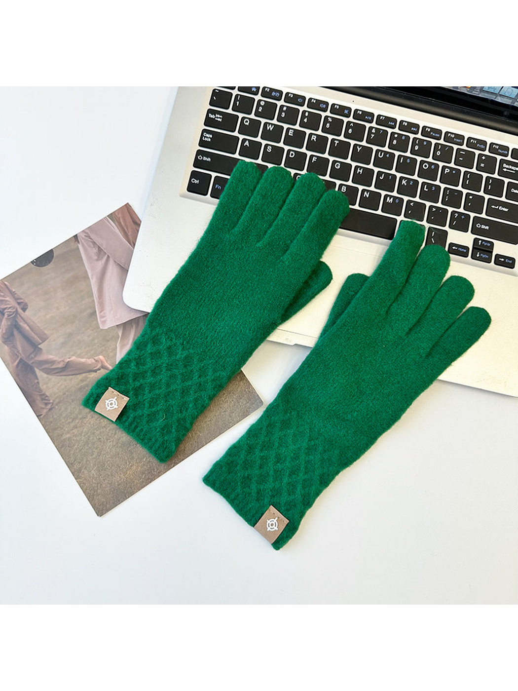 Green knit gloves with diamond lattice cuffs arranged beside a laptop.