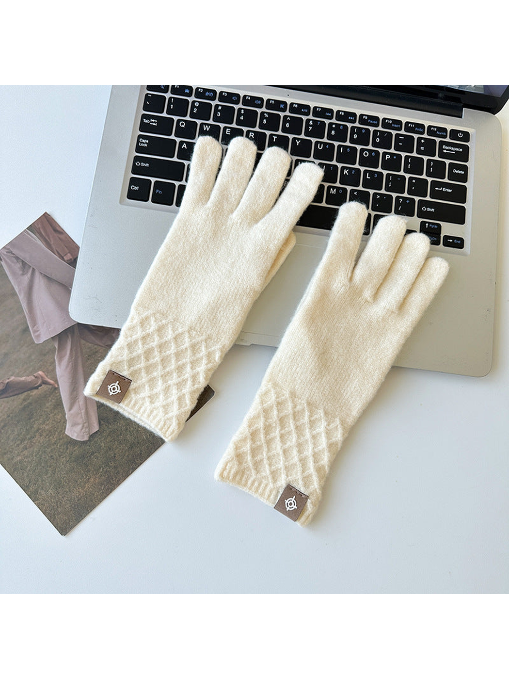 Ivory knit gloves with diamond lattice cuffs arranged beside a laptop.