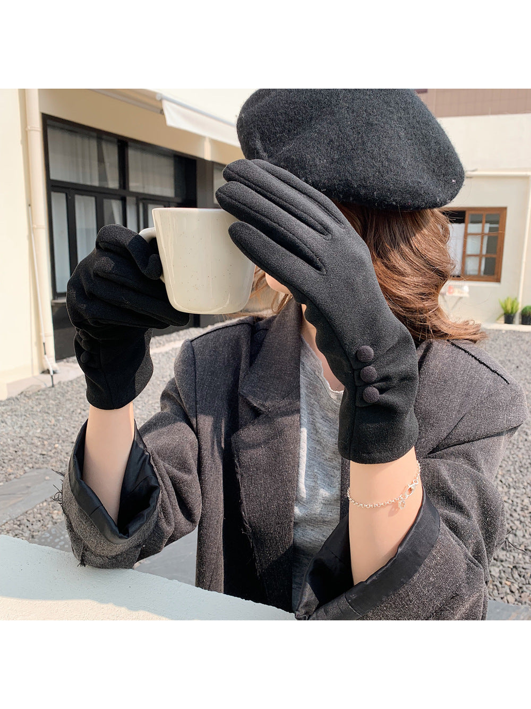 Black gloves with three button accents worn while holding a mug outdoors.