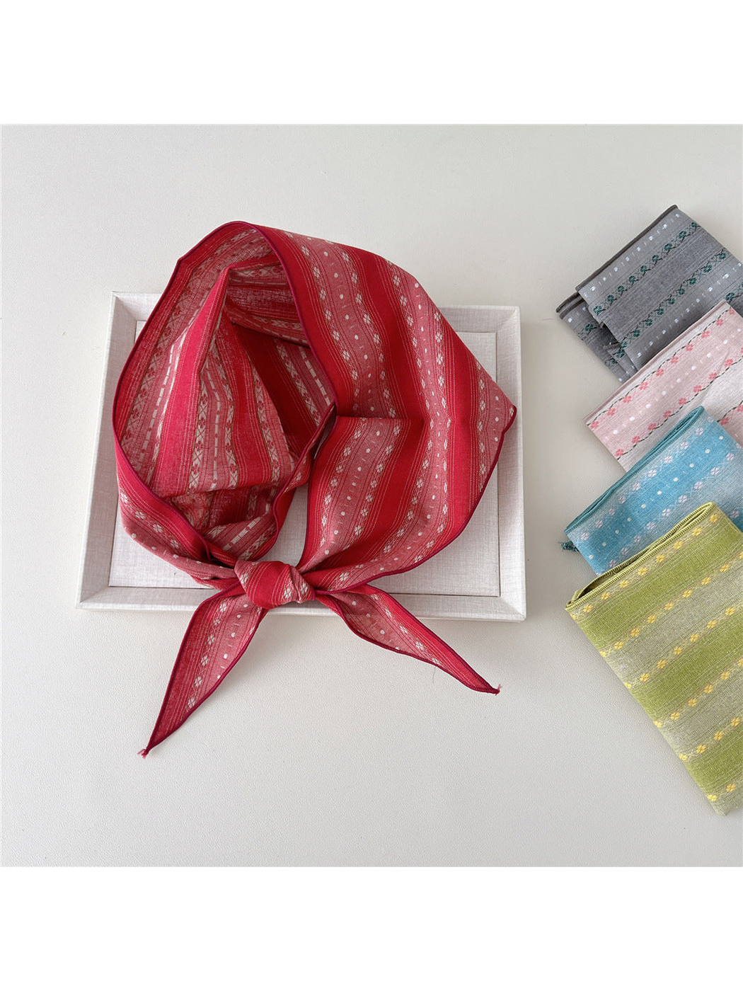Red floral triangle scarf displayed with folded gray, pink, blue, and yellow colorways