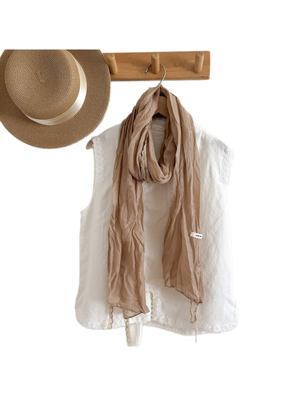 Beige lace-edged scarf draped over a white top on a clothing rack