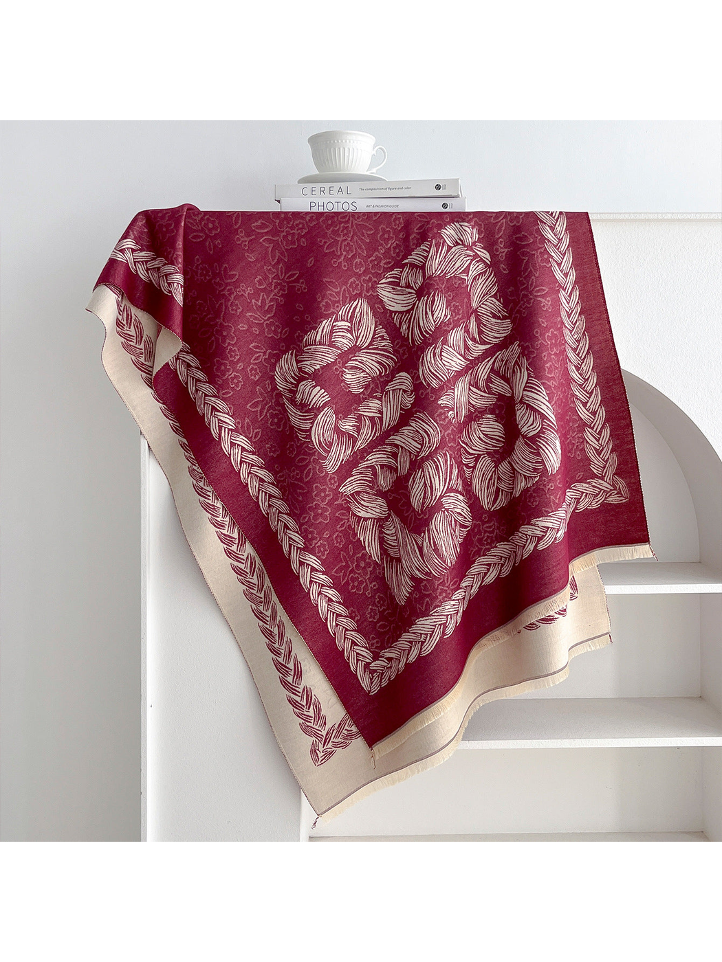 Burgundy scarf with floral motifs and a braided border draped over a shelf