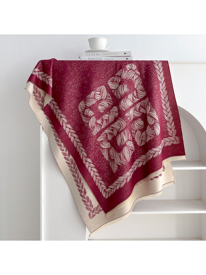 Burgundy scarf with floral motifs and a braided border draped over a shelf
