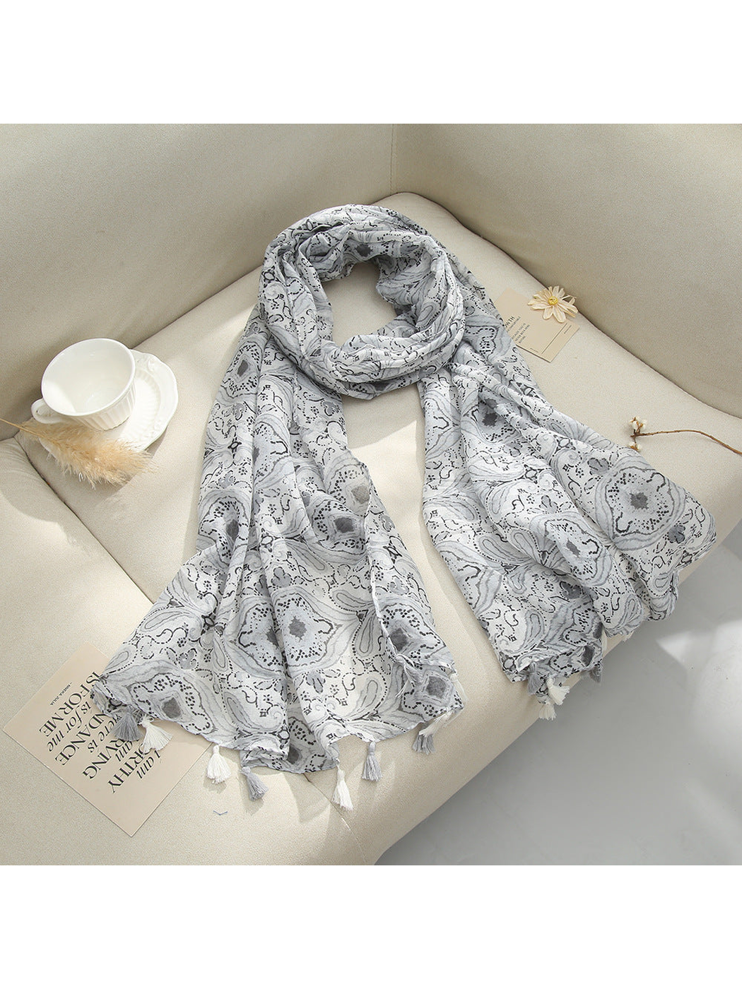 Gray paisley scarf with tassel fringe arranged on a sofa