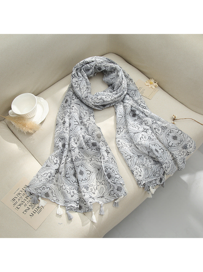Gray paisley scarf with tassel fringe arranged on a sofa