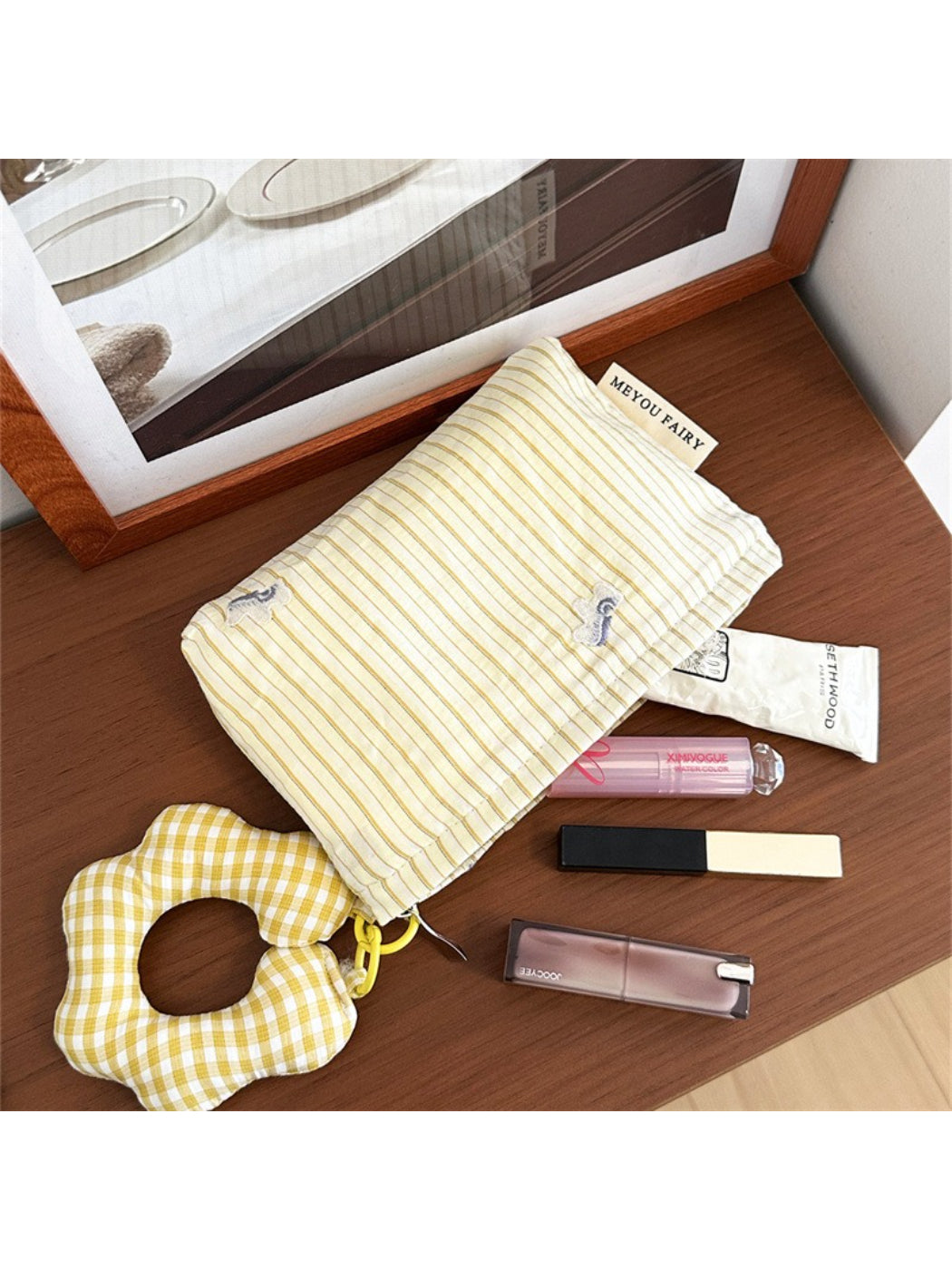 Striped cosmetic bag with plush charm next to makeup brushes