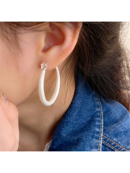 Glossy color hoop earrings worn on a model's ear