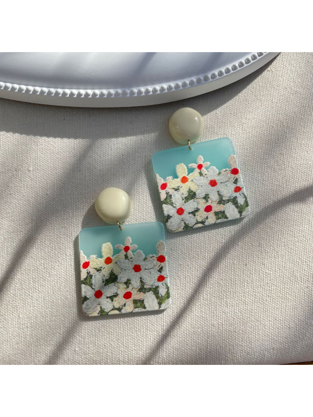 Close-up of Earwish Daisy Field drop earrings with white daisy petals and yellow centers
