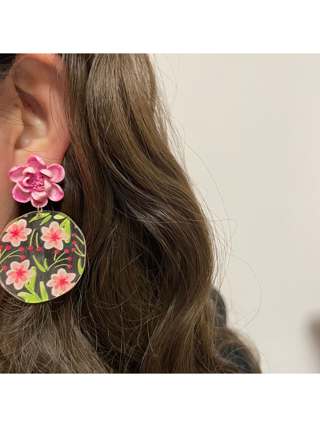 Earwish Garden Flower Disc Earrings displayed on a jewelry stand with green leaves