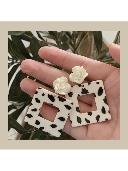 Earwish Cow Print Rose Earrings front view with black and white cow pattern and pink rose detail