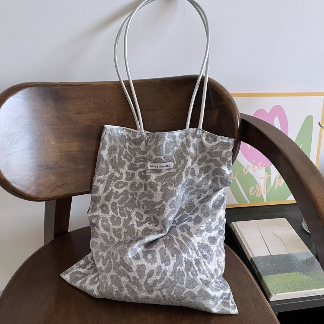 Grey tote bag with leopard print pattern and black handles on white background